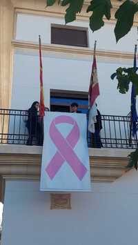 La junta local de la AECCcoloca un lazo rosa en el balcón del Ayuntamiento.